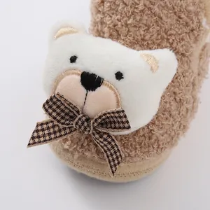 Macro detail view of a soft baby winter shoe with fuzzy bear face and brown plaid bow tie.