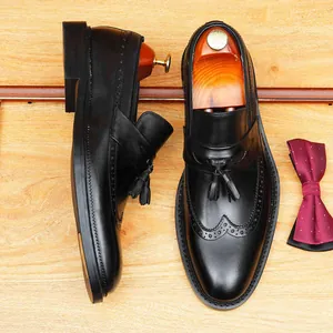 Black leather tassel loafers for men with elegant brogue detailing on wooden surface