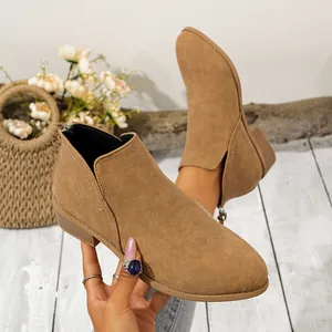 Primer plano de botines de ante beige con punta fina, tacón bajo grueso y cremallera