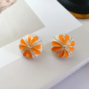 Nahaufnahme von Vintage-Emaille-Ohrsteckern mit orangefarbenem und weißem Emaille-Detail