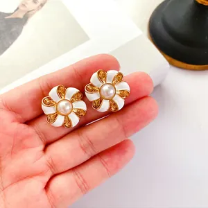 Gros plan de boucles d'oreilles fleurs en émail vintage avec perle sur la main