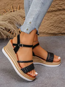 Détail de sandales compensées noires à brides tressées avec semelle plateforme et boucle cheville