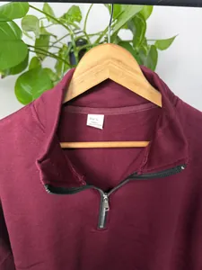 Detailopname van een bordeauxrode herentrui met opstaande kraag, rits en maatlabel L