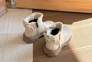 Close-up detail of beige girl's princess boots featuring elegant bow and pearl trim