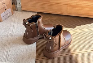 Detail showing the brown leather kids' boots with decorative bow and pom-poms