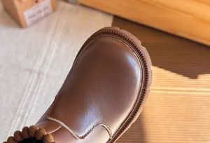 Close-up detail of brown leather girls' Martin boot showing fine stitching and texture.