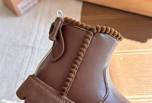 Close-up detail of brown leather children's boot with cute pom-pom trim.