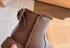 Close-up of brown children's boots featuring pom-pom trim and a side bow detail