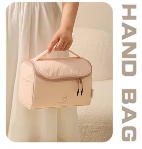 Vue détaillée d'une trousse à maquillage en nylon rose pêche tenue par un modèle