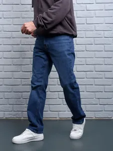 Detail side view of men's loose straight-leg summer jeans against a grey brick wall