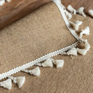 Close-up detail of a rustic jute placemat featuring decorative white tassel fringe.