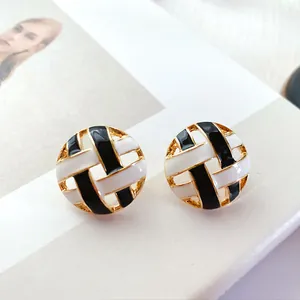 Close-up of vintage round hollow-out enamel stud earrings with black and white woven pattern.