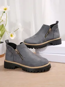 Détail de bottines grises en daim à talon épais avec fermeture éclair latérale dorée.