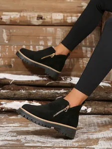 Gros plan de bottines en daim noir avec fermeture éclair dorée portées par un mannequin sur bois