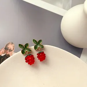 Nahaufnahme von roten Beeren-Ohrsteckern mit grünen Emaille-Blättern auf Keramikteller.