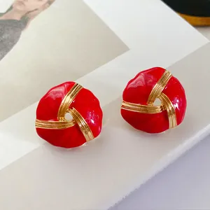 Close-up of red enamel knot stud earrings with gold-tone accents on a white surface