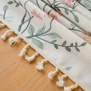 Detailed macro view of elegant floral embroidery and white tassel fringe on a linen tablecloth