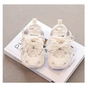 Detailed view of lace butterfly bow and pearl accents on white girls' mesh sneakers.