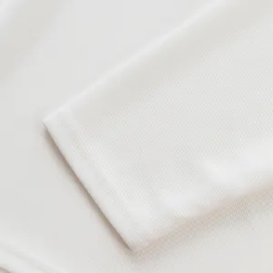 Gros plan sur la texture maille côtelée française raffinée du poignet d'un polo blanc pour homme.