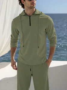 Detail view of a men's olive green linen hoodie and trousers set in a coastal setting