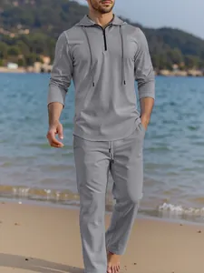 Man walking on beach wearing a grey hooded linen-style set with zipper detail.