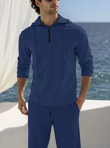 Close-up of a man wearing a navy blue hooded linen set on a sunny seaside balcony.