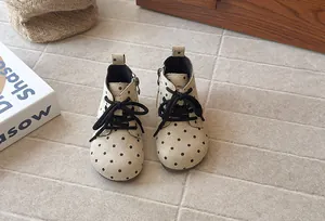 Front view of girls' beige polka dot ankle boots with black laces and side zippers.