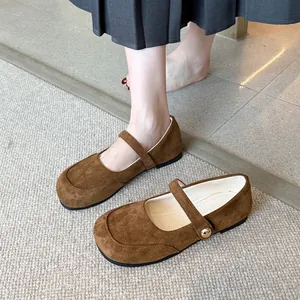 Gros plan de ballerines Mary Jane en daim marron avec boucle en métal sur tapis.