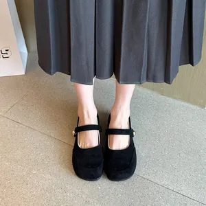 Gros plan de chaussures Mary Jane en daim noir portées avec une jupe plissée élégante.