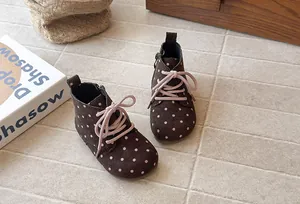 Detailed view of brown polka dot children boots with pink laces on neutral tile floor