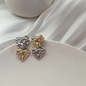 Macro view of textured heart-shaped stud earrings with wrinkled gold and silver finish