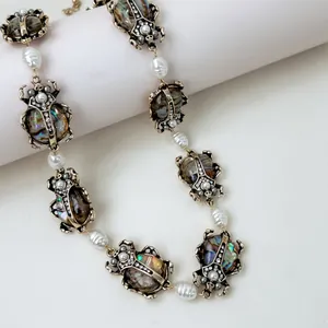Dettaglio di ciondoli a scarabeo vintage e perle barocche su una collana oro antico.