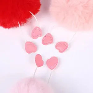 Detailed view of fluffy faux fur pom-poms featuring pink heart-shaped leather accents
