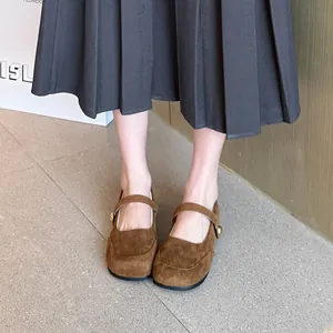 Vue détaillée de chaussures Mary Jane en daim marron portées avec une jupe plissée.