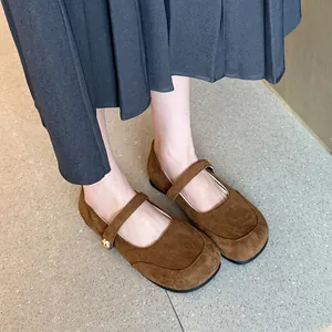 Gros plan de ballerines Mary Jane en daim marron portées avec une jupe plissée élégante.