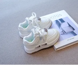 Vista detallada de zapatillas blancas para niñas con dijes de peces en alfombra gris