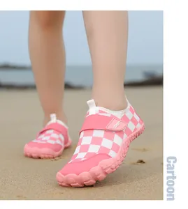 Detail view of pink and white checkered aqua shoes worn by a child on a beach.