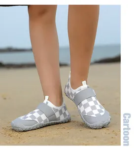 Close-up of children's grey and white checkered water shoes being worn on a sandy beach.