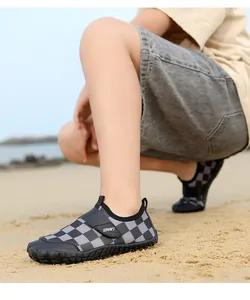 Detail view of children's grey checkerboard wading shoes with anti-slip soles on a beach.