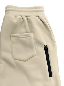 Detalle de pantalones deportivos beige con bolsillo lateral de cremallera y trasero.