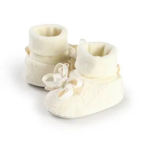 Close-up of cream baby lace socks with a silk bow and ribbed cuffs