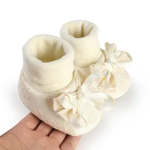 Detail showing cream lace baby socks featuring large satin ribbon bows and soft ribbed cuffs