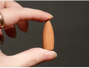 Macro detail of a brown sandalwood backflow incense cone held between fingers for scale