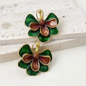 Vue détaillée de boucles d'oreilles vintage en émail avec fleurs vertes et marron sur pierre.
