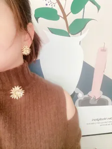 Model trägt barocke goldene Sonnenblumenbrosche und passende Ohrstecker auf braunem Pullover.