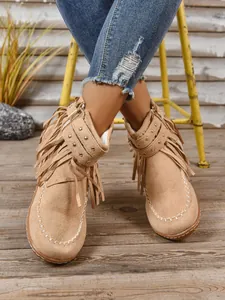 Detailopname van bruine suède enkellaarsjes met franjes, studs en western-stiksel.
