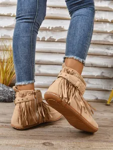 Detailopname van beige suède enkellaarzen met franjes en western-stijl gesp detail.