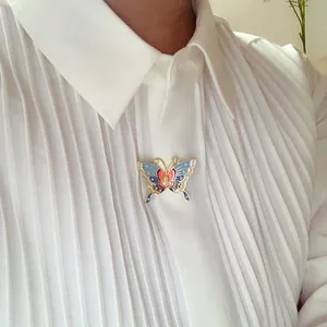 Elegant enamel butterfly brooch with pearls pinned on a white pleated shirt detail view