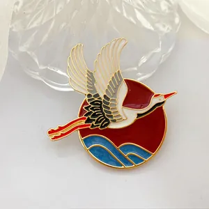 Detalle de un broche de estilo chino con una grulla, sol rojo y olas azules.