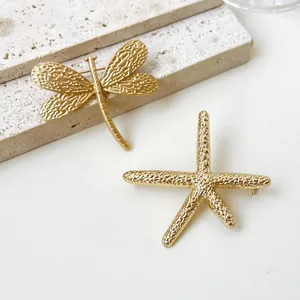 Detailansicht von goldenen Libellen- und Seestern-Broschen mit strukturierter Oberfläche.